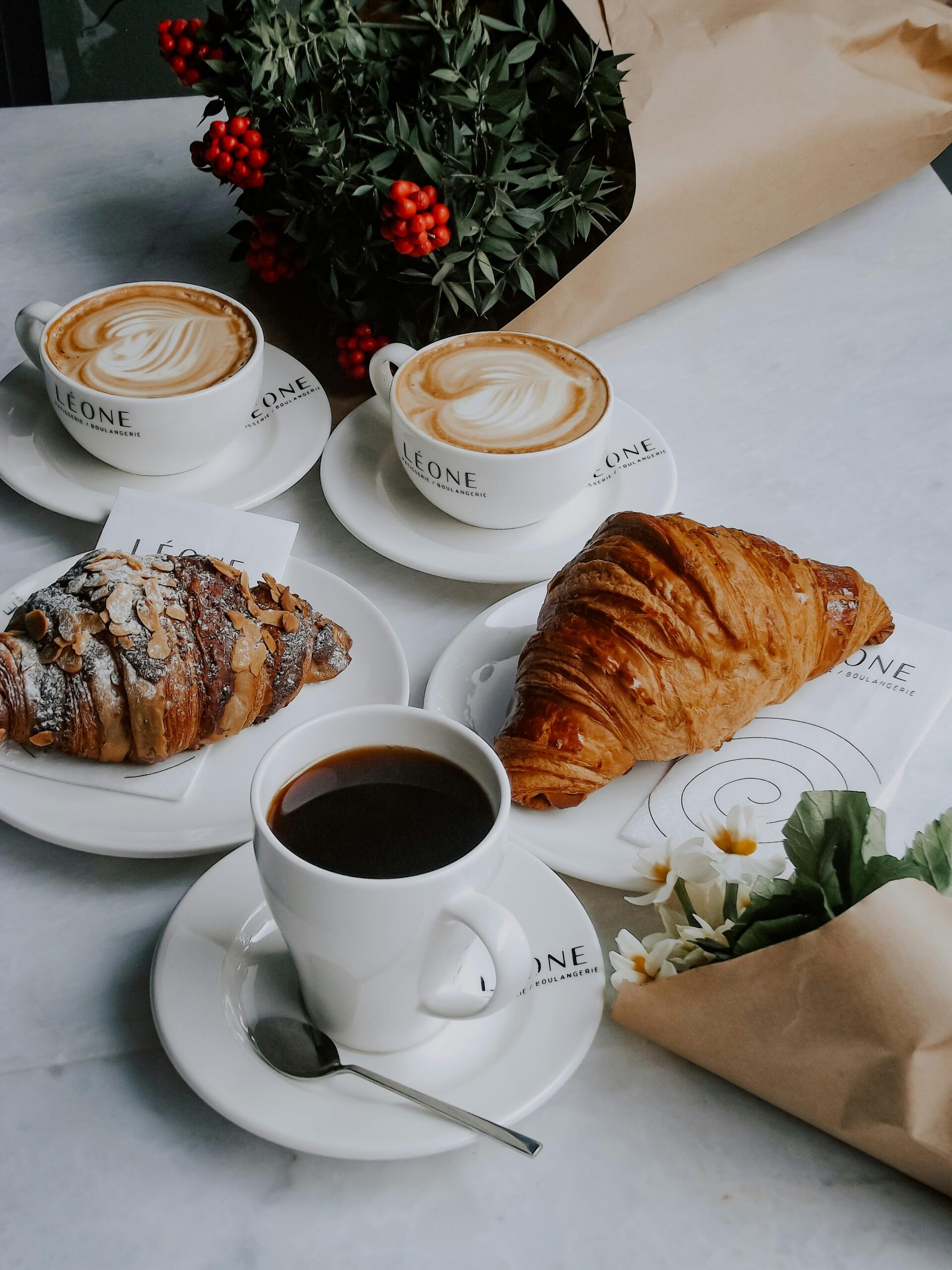 Elegant French breakfast setting with coffee, cappuccino, croissants, and flowers on marble table.