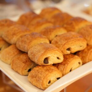 Delicious golden brown chocolate croissants beautifully arranged on a white platter for breakfast or catering event.