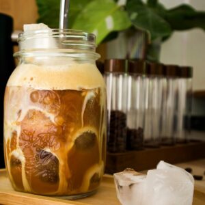 Close-up of a delicious iced coffee in a mason jar with a straw on a wooden tray.
