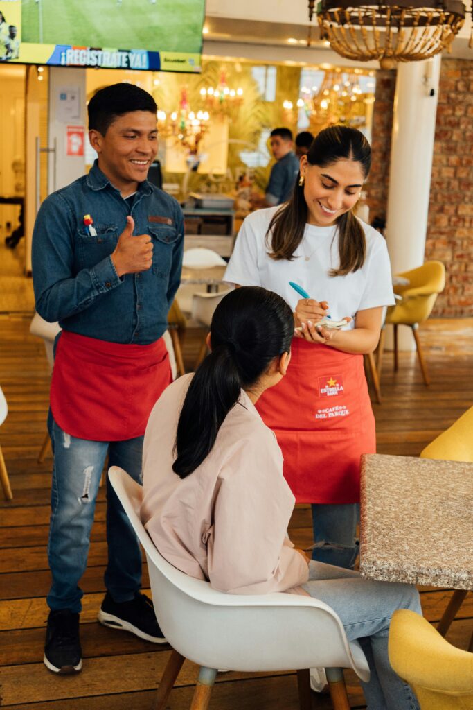 Smiling waitstaff taking an order from a customer in a cozy cafe setting.