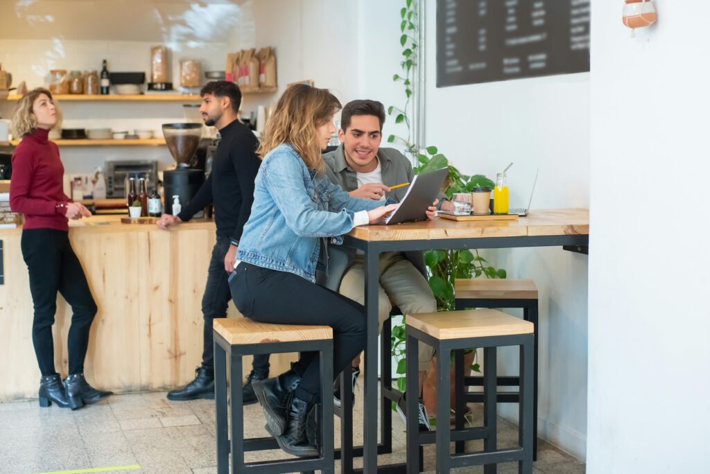 Professionals collaborating over a laptop in a lively Portuguese café setting.